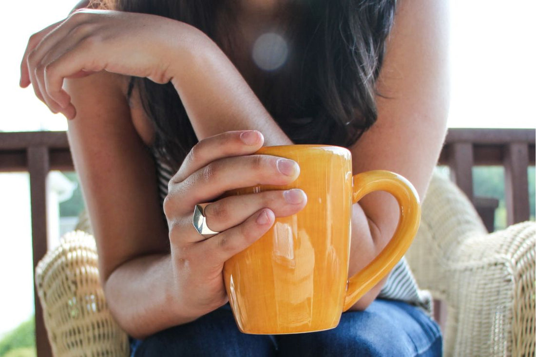 woman business owner holds a cup of coffee in orange ceramic mug